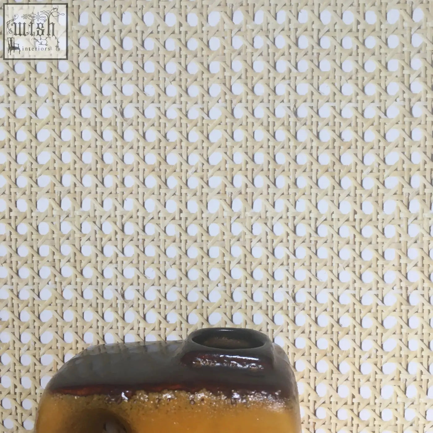 A ceramic vase with glossy amber base and dark brown rim shown on a woven cane wallpaper background