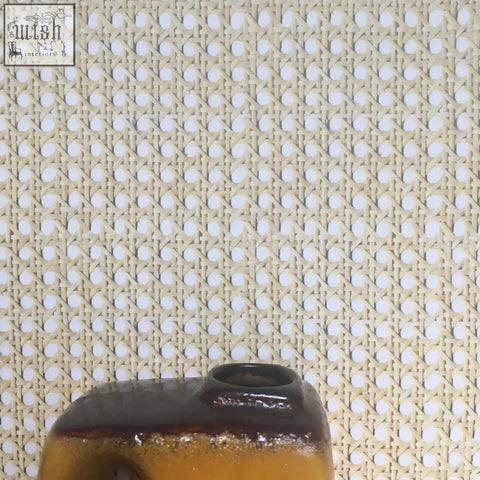 A ceramic vase with glossy amber base and dark brown rim shown on a woven cane wallpaper background