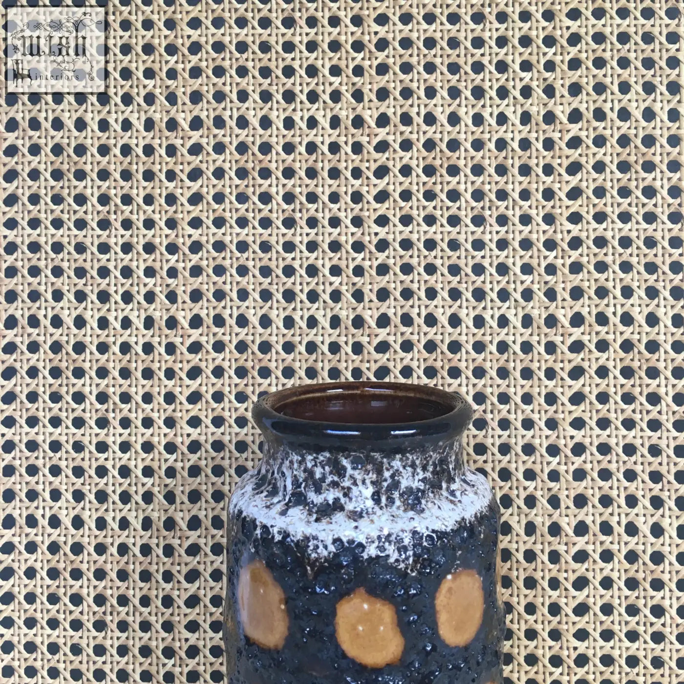 A dark blue ceramic vase with speckled glaze and tan accents on woven cane wallpaper background