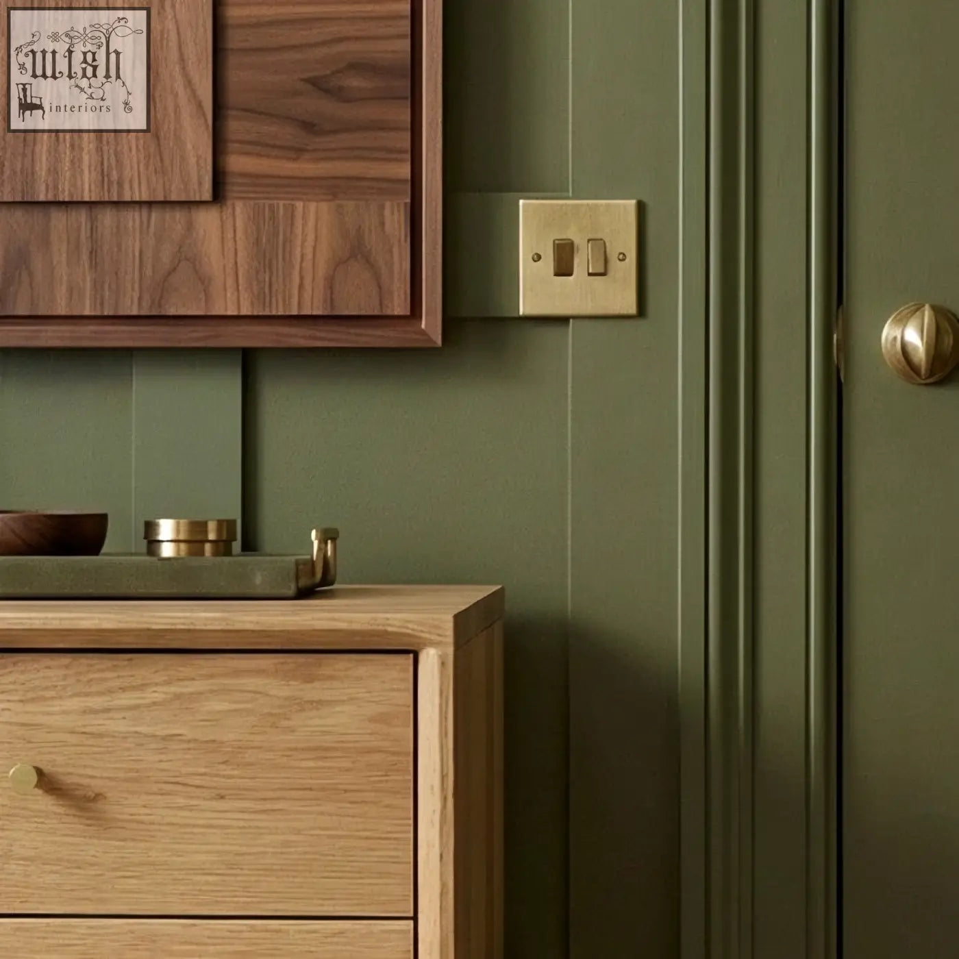 Gold-colored double light switch on olive green wall next to solid oak wright oak bedside table