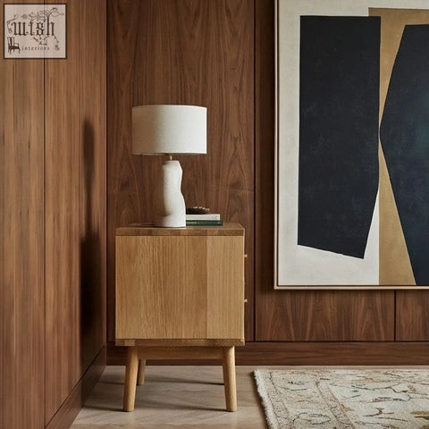 A minimalist white ceramic table lamp with sculpted base and linen shade on a solid oak wright oak bedside table