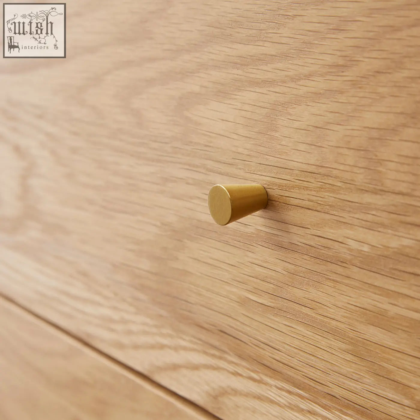 A sleek gold-toned brass drawer pull on a wright oak chest of 3 drawers with oak veneers and light wood grain