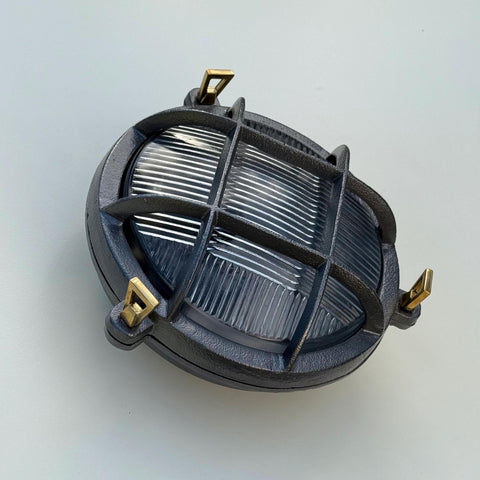 Dark gray cast iron oval wall light with brass brackets and ribbed glass panels a nautical bulkhead wall light