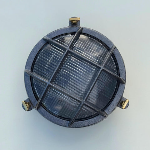 Dark gray industrial wall light with ribbed glass panel and brass hardware perfect as a nautical bulkhead wall light