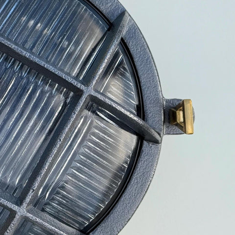Gray textured metal nautical bulkhead wall light with ribbed glass panels and brass accent in industrial style