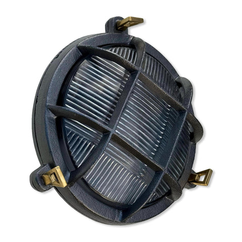 Dark gray cast iron wall light with brass hardware and ribbed glass panel in a nautical bulkhead wall light design