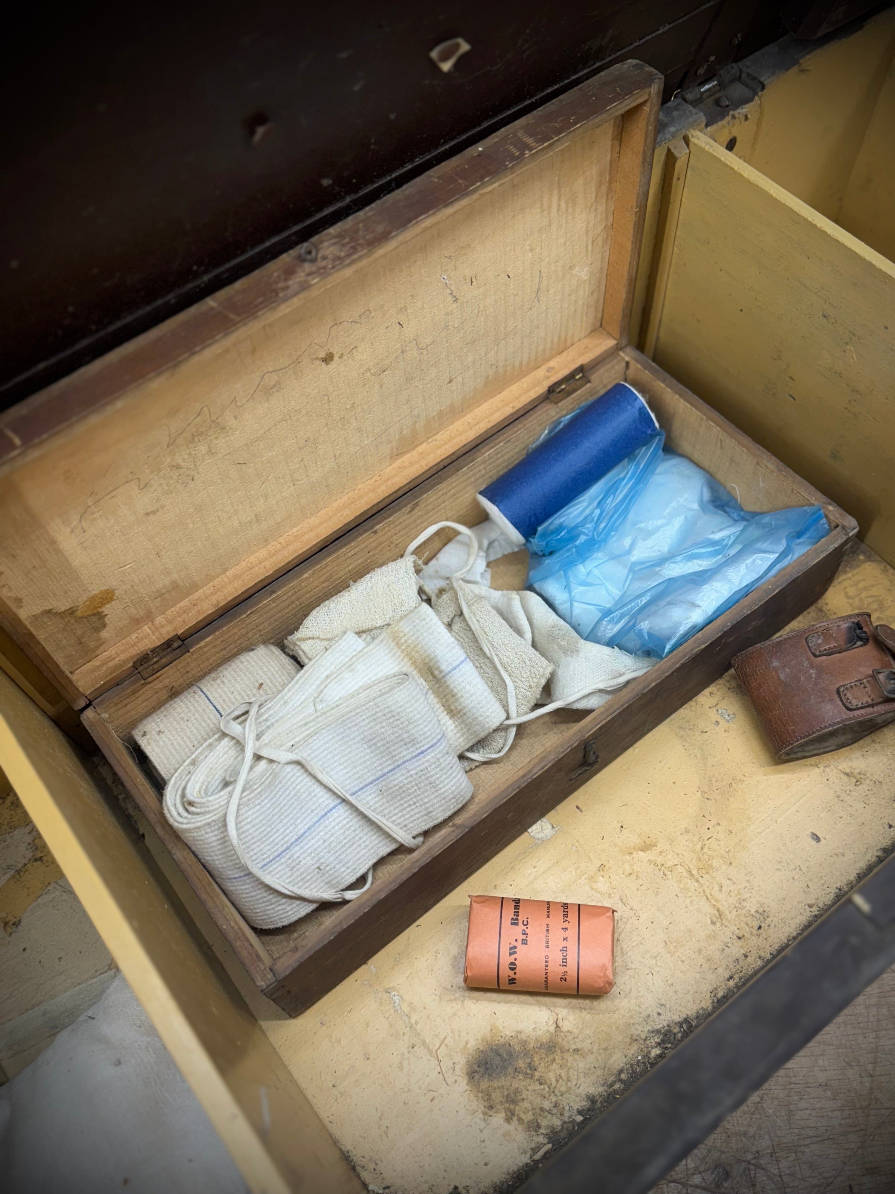 Weathered wooden WWII red cross aid box with hinged lid holding white cloths and blue plastic civil defence items