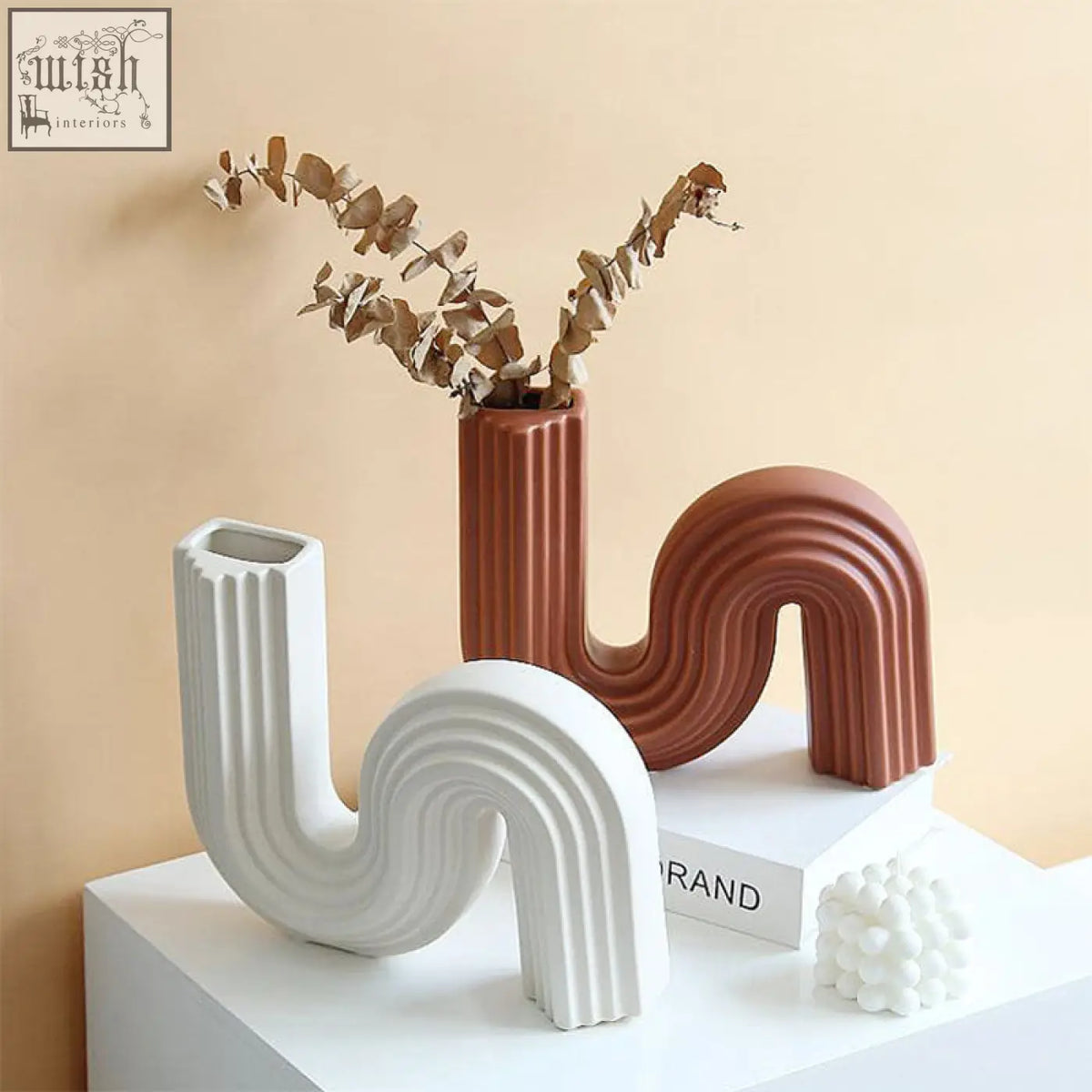 A terracotta ceramic shaped vase with a ribbed s-shaped design holding dried eucalyptus called xenia ceramic shaped vase