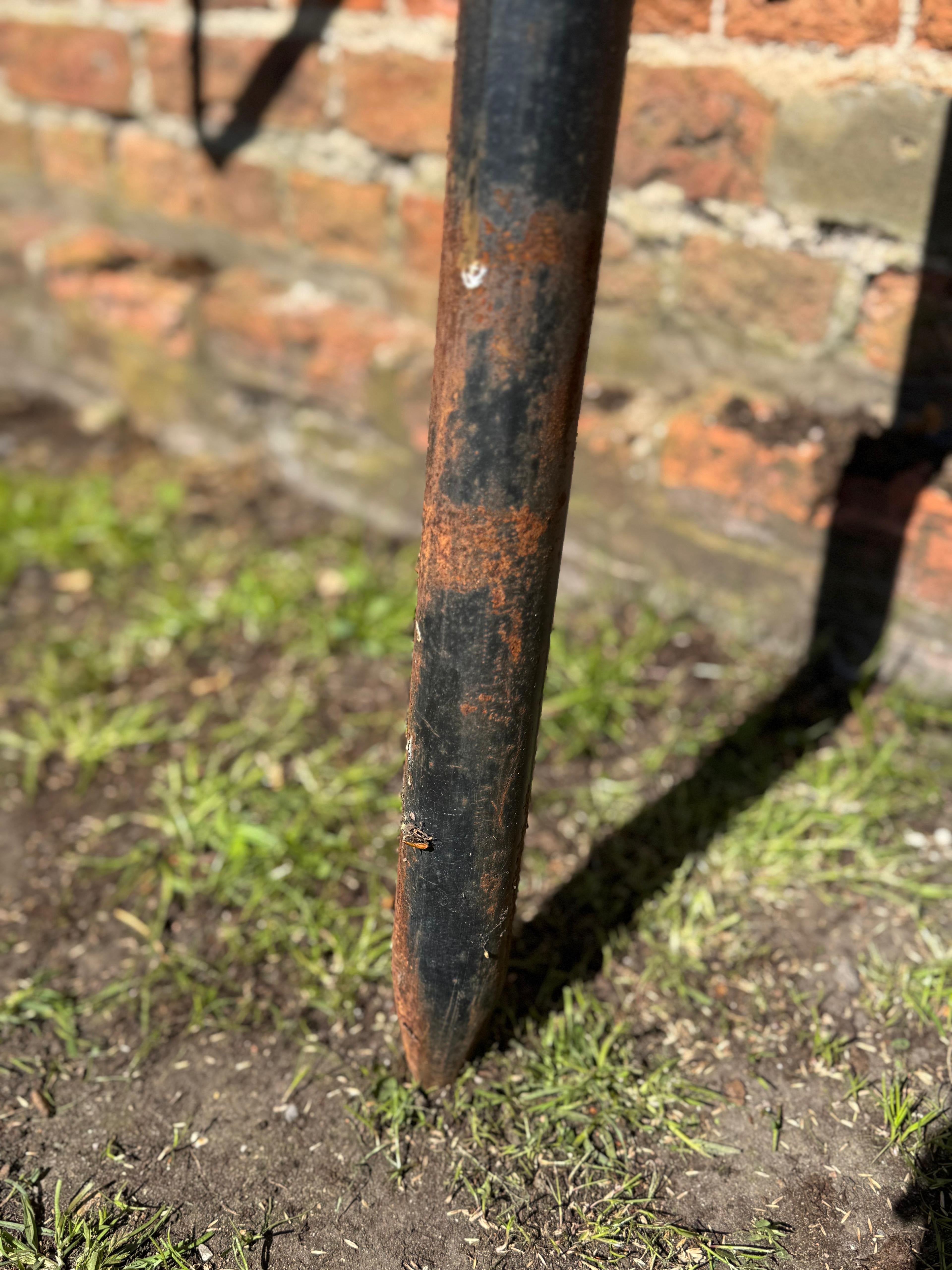 A weathered black metal star garden stake with rust streaks and a pointed tip standing in grass by a brick wall