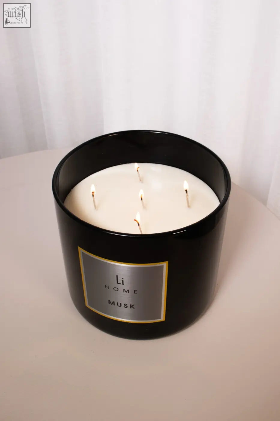 Black cylindrical xl candle jar with five lit white musk candles and silver label li home musk