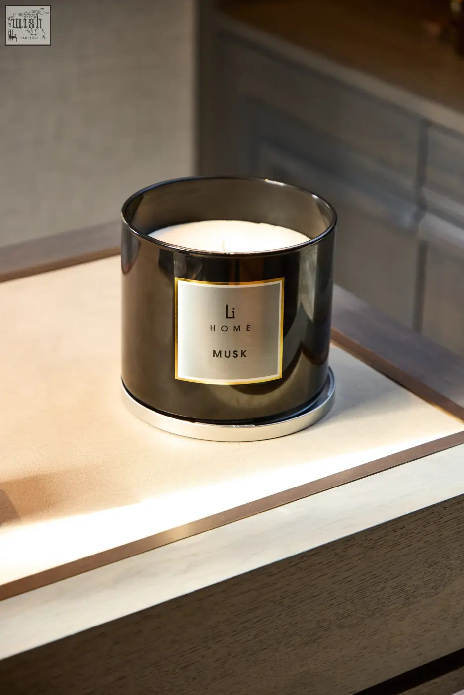 A sleek dark metallic cylindrical xl candle holder with white wax and a gold label reading li home musk white musk