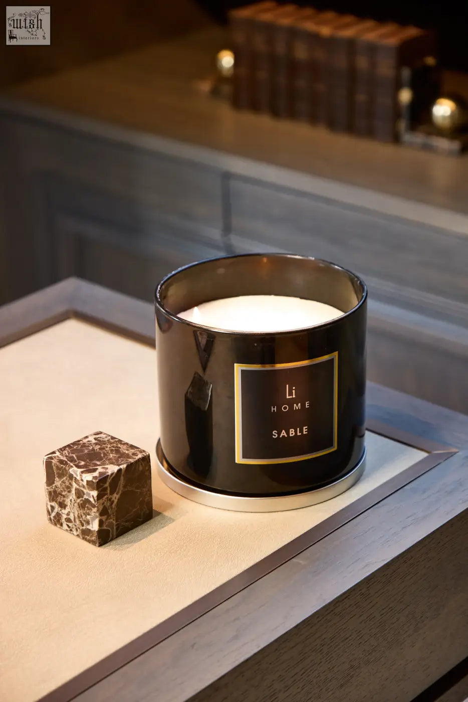 Black cylindrical xl candle sable with gold foil label and silver rim next to a brown marble cube