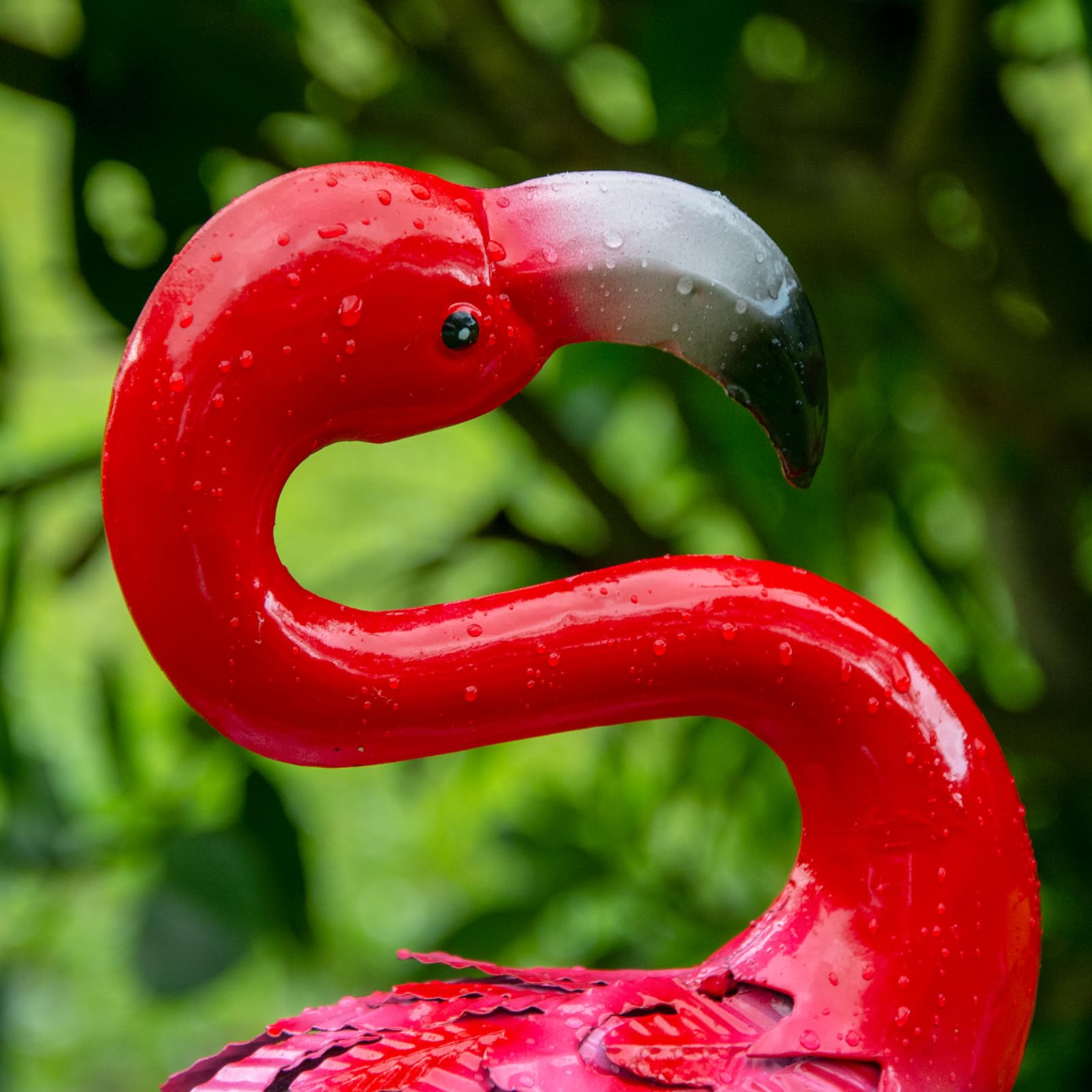 A glossy red metal flamingo statue with white and black beak and water droplets for outdoor garden decor