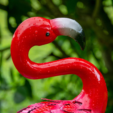A glossy red metal flamingo statue with white and black beak and water droplets for outdoor garden decor