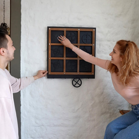 Black and wood-framed wall-mounted tic tac toe game with a circular metal wheel in the xox board three in a row product