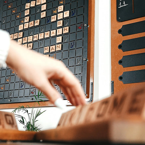 A wooden scrabble board with letter tiles on a dark grid framed by light wood for a classic word game to boost vocabulary skills
