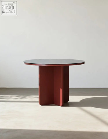 Yadav glass top dining table is a round accent table with a dark glass top and bold red lacquered geometric base