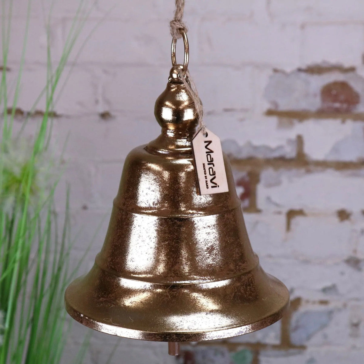 A rustic gold-finished metal yanika hanging bell with textured surface and rope loop featuring a marav tag