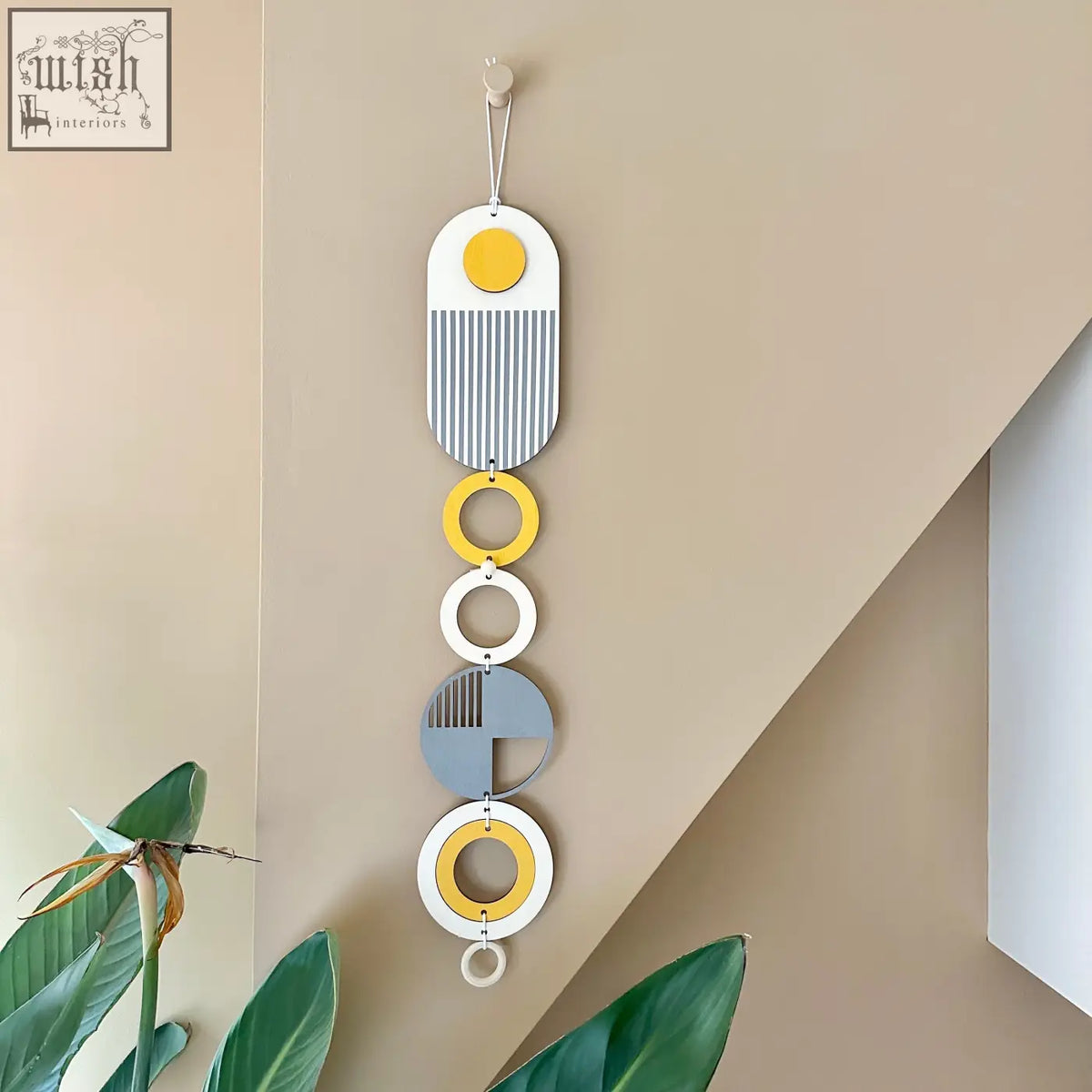 A modern wall hanging with vertical ochre yellow, gray, and white oval and circle shapes featuring striped patterns