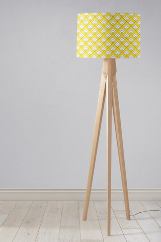 A modern tripod table lamp with a bright yellow and white geometric design lampshade and light wooden legs