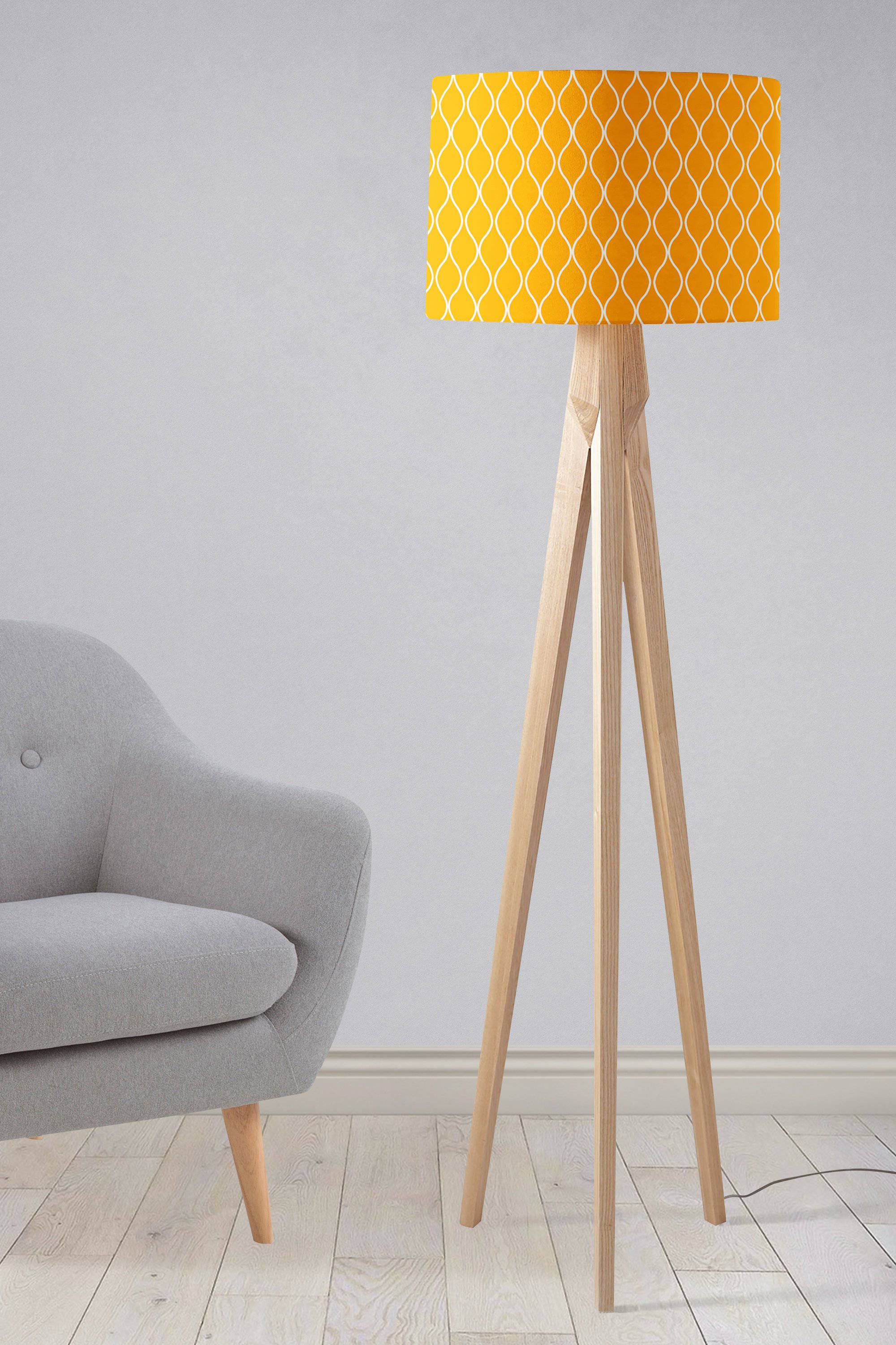 A vibrant yellow lampshade with white geometric design on slender wooden tripod table lamp legs