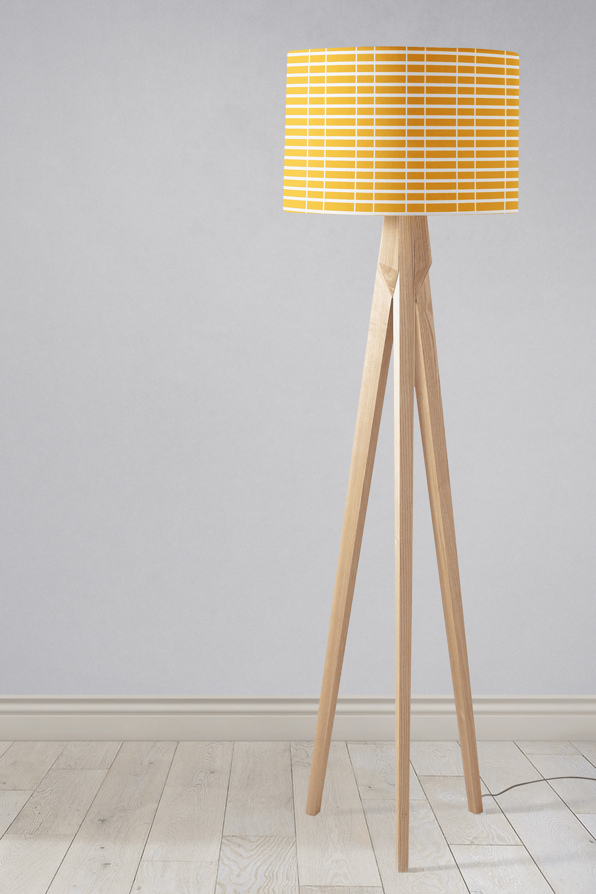 A modern tripod table lamp with a yellow lamp shade featuring white geometric stripes and light wooden legs