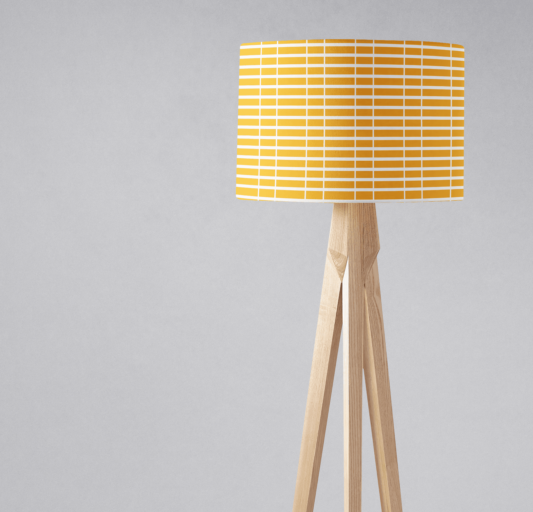 A modern tripod floor lamp with a yellow and white geometric lamp shade and light wooden legs perfect as a table lamp