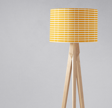 A modern tripod floor lamp with a yellow and white geometric lamp shade and light wooden legs perfect as a table lamp