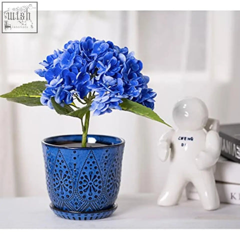 Vibrant blue beaded ceramic planter with lace pattern and drain holes holding artificial hydrangeas for indoor outdoor use