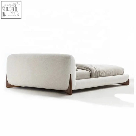 Modern yukina bed with sculptural frame wrapped in soft beige upholstery and sleek dark wood legs