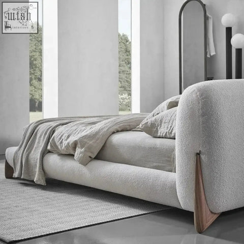 Modern yukina bed with plush light gray textured fabric and sleek wooden legs featuring a sculptural frame wrapped design