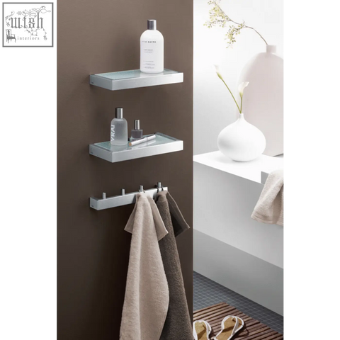 Modern chrome linea bathroom shelf with glass surface holding toiletries and towels in brushed stainless steel