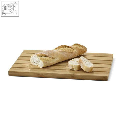 A light brown oiled bamboo panas breadboard with parallel slats holds a golden-brown baguette and stainless steel tray