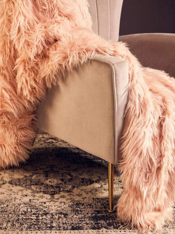 A beige zamora mink velvet accent chair with gold finish legs draped with a plush peach faux fur throw
