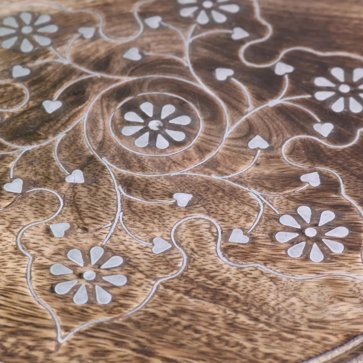 A wooden tray with intricate inlaid floral and heart patterns on the zanskar small hand carved side table