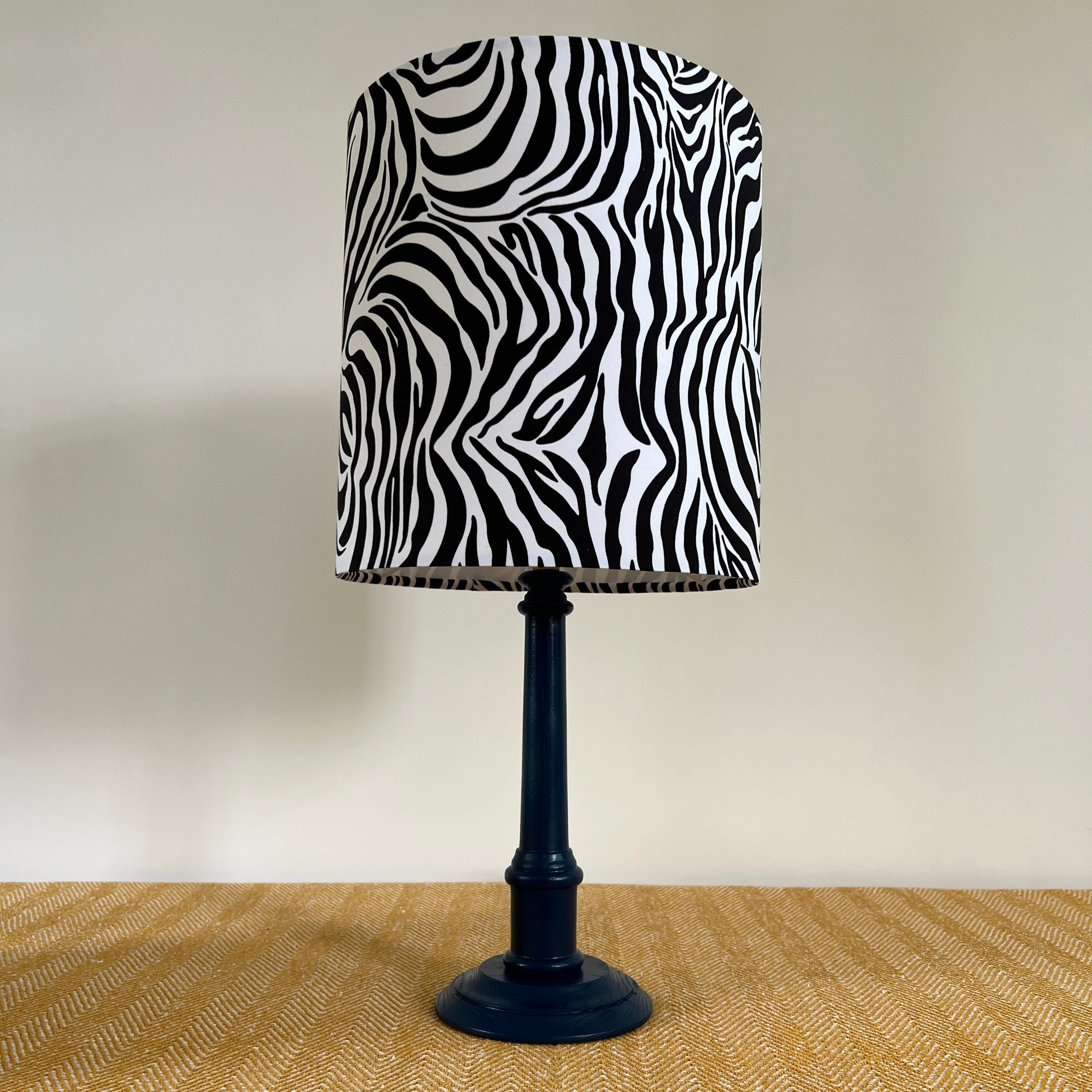 A navy blue table lamp with a 30cm height zebra cotton drum lampshade featuring a ceiling shade fitting that sits 3-4cm