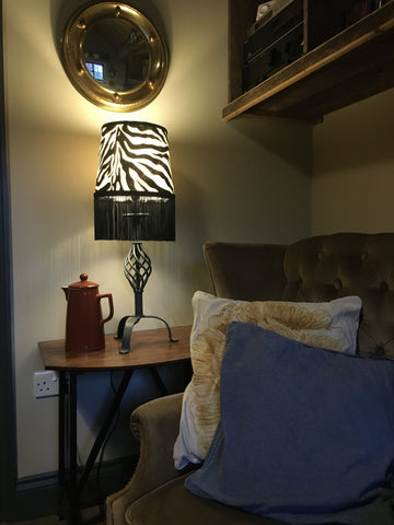 Zebra print velboa french drum lampshade with black fringe, braid, and dark metal base for stylish lighting