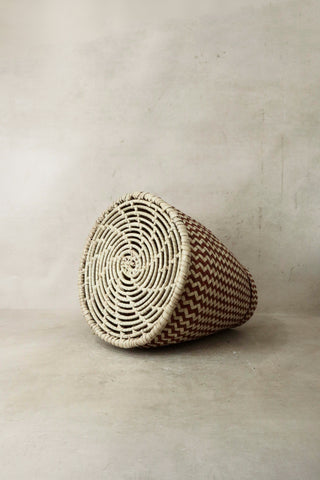 A handwoven tapered planter basket in brown and cream with a zigzag pattern and cream-colored rim from Malawi