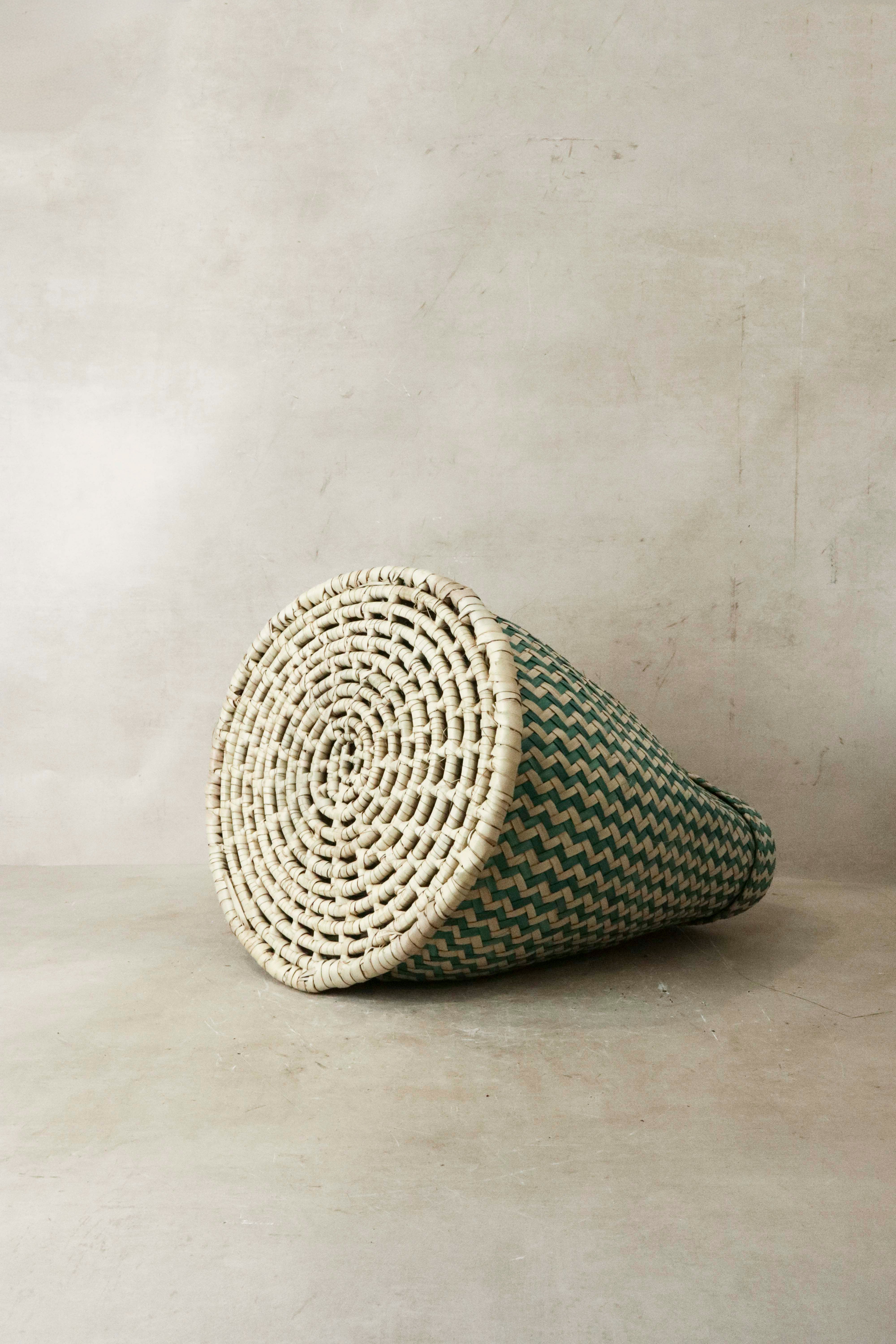 A handwoven green and cream zigzag patterned planter basket from Malawi with a circular woven base