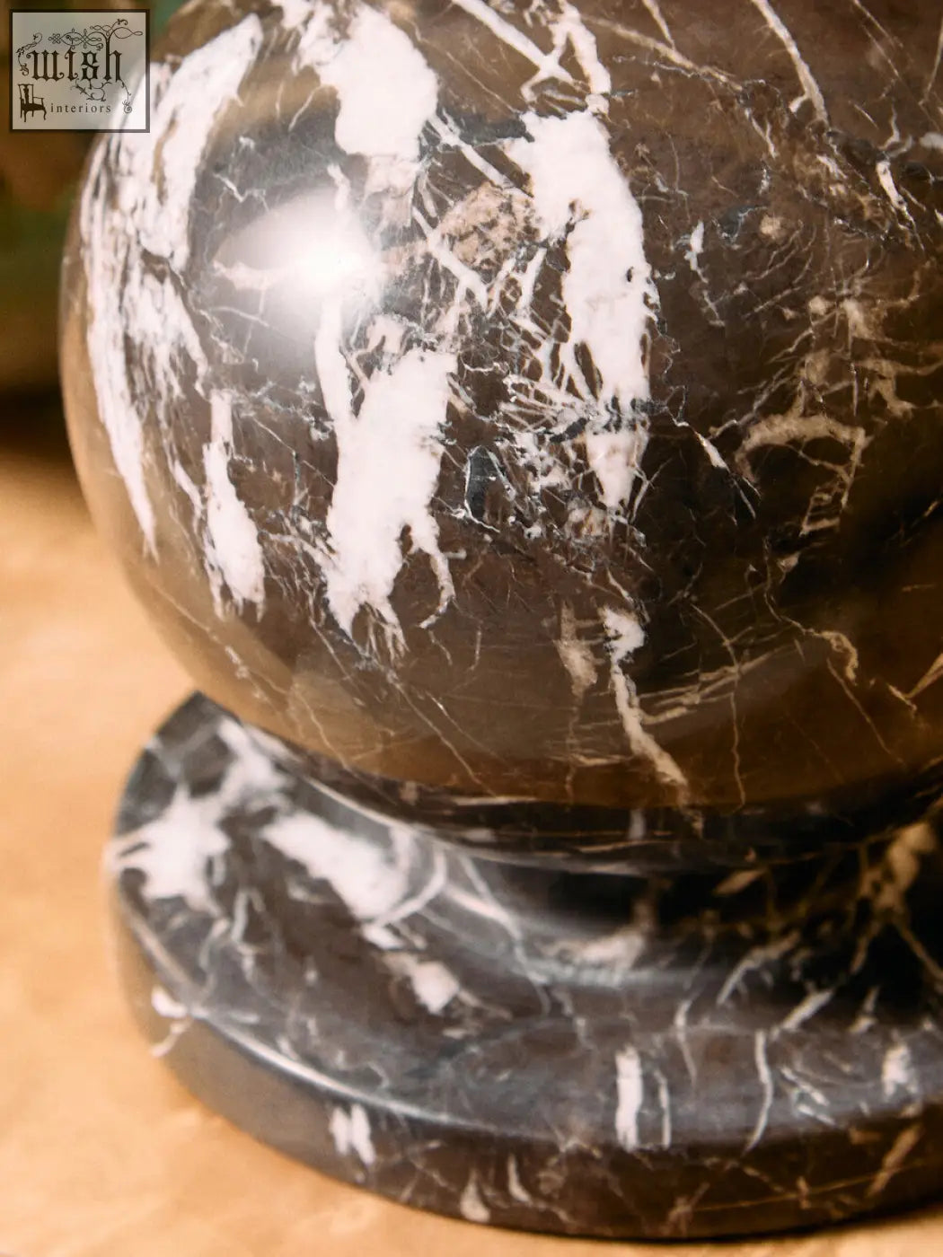 A polished dark brown marble ball sculpture with striking white veined detail resting on a matching base