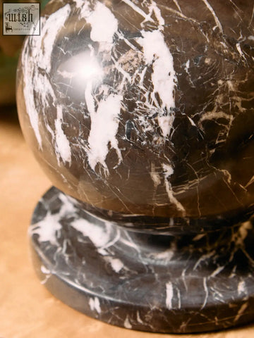 A polished dark brown marble ball sculpture with striking white veined detail resting on a matching base