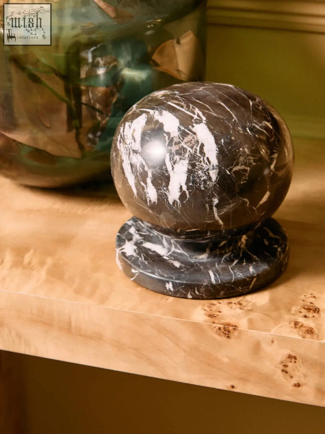 A sleek black and white veined marble ball sculpture resting on a matching dark marble base