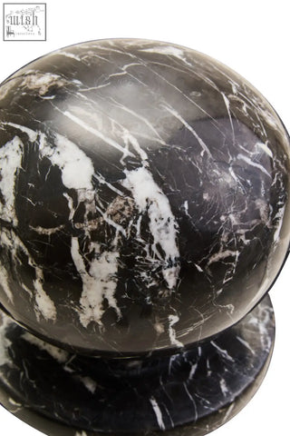 A sleek black marble ball sculpture with white veined details resting on a matching circular base
