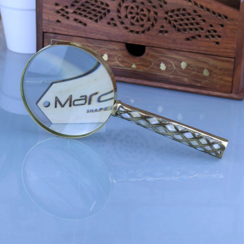 A zuari brass magnifying glass with a decorative lattice handle and clear round lens featuring mother of pearl accents